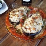 Berenjenas rellenas de pechuga de pollo y verduras, horneadas y servidas en fuente de cristal con tomate fresco y hierbas aromáticas.