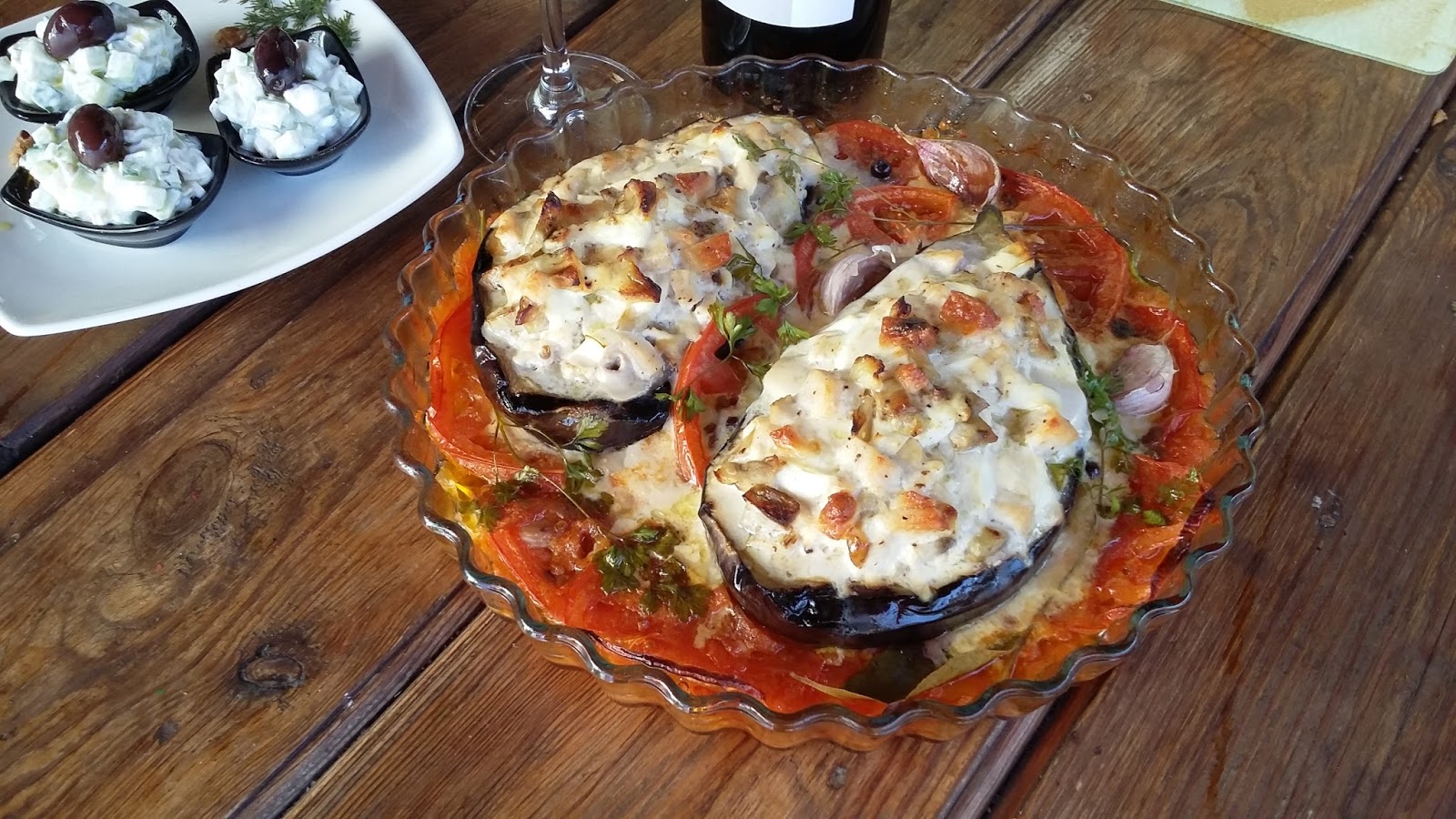 Berenjenas rellenas de pechuga de pollo y verduras, horneadas y servidas en fuente de cristal con tomate fresco y hierbas aromáticas.