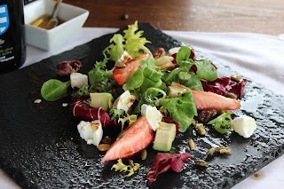 Plato de ensalada gourmet con queso de cabra, fresas, nueces y hojas verdes servido en fuente blanca