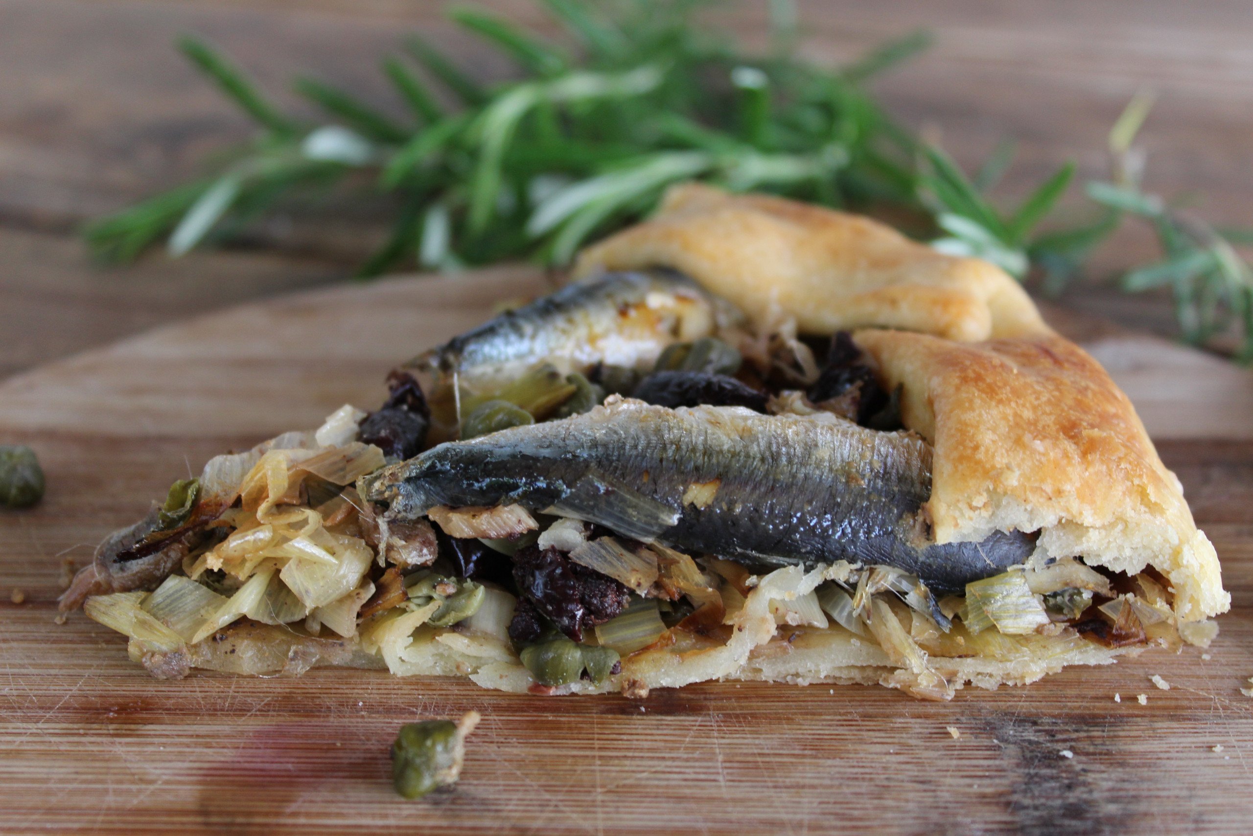 Coca artesanal con sardinas enteras, puerro dorado, olivas negras y alcaparras sobre masa crujiente