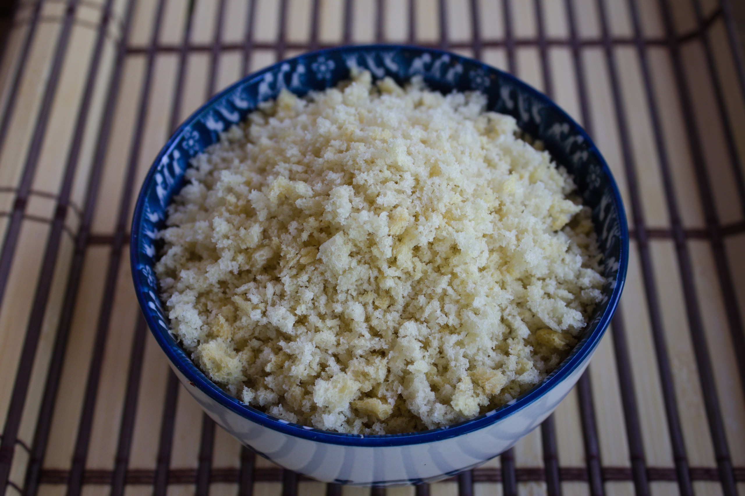 Pan rallado panko en un cuenco azul decorativo sobre esterilla de bambú, mostrando su textura ligera y crujiente.