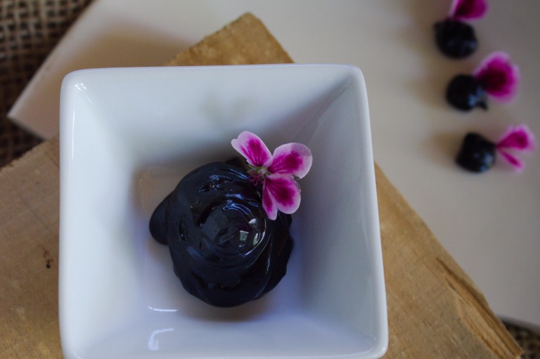 Alioli de ajo negro en presentación gourmet con flores comestibles sobre plato blanco.