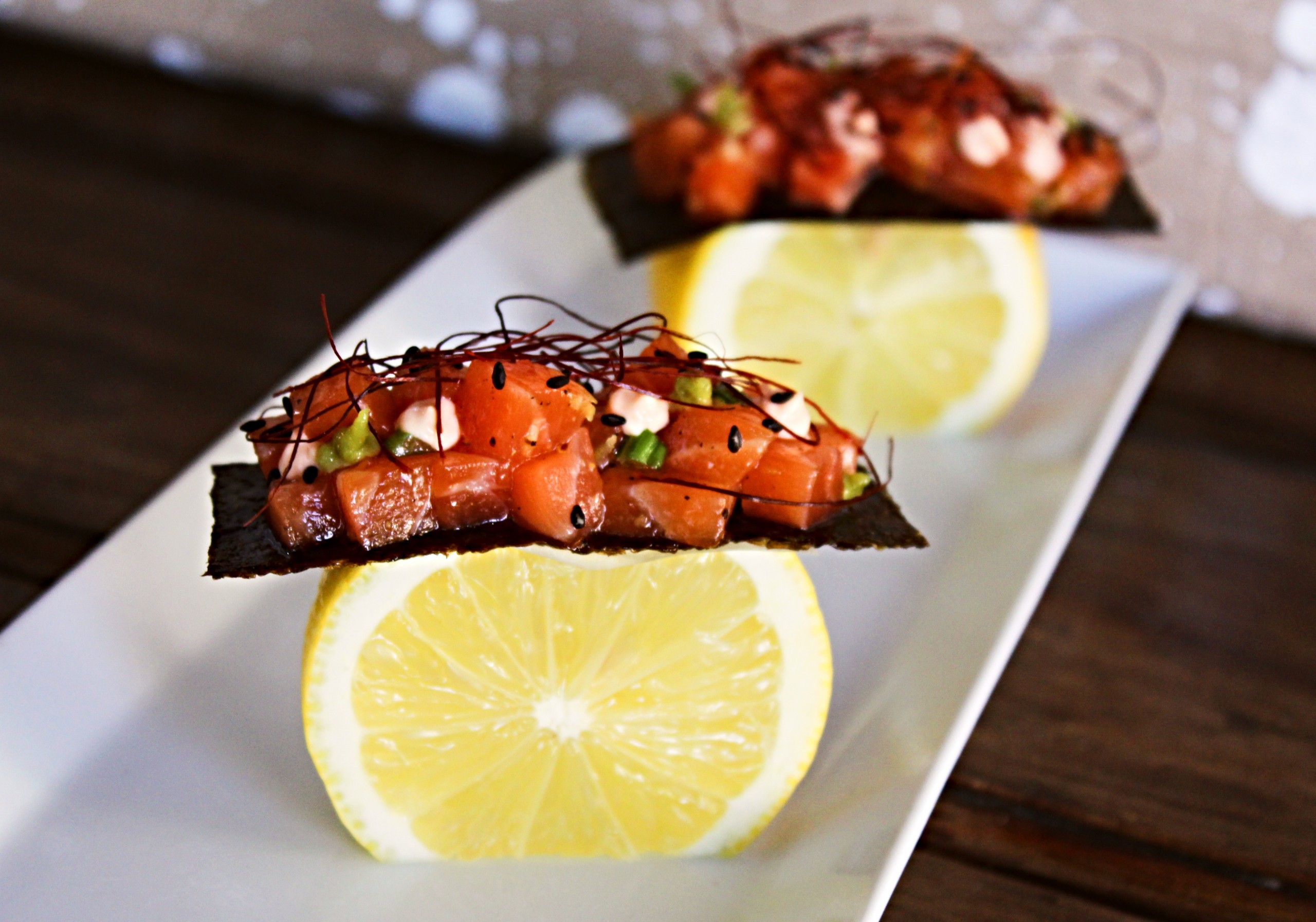Tartar de salmón sobre limón y alga nori crujiente, decorado con wasabi, sésamo negro, hilos decorativos hito togarashi y aderezo cremoso.