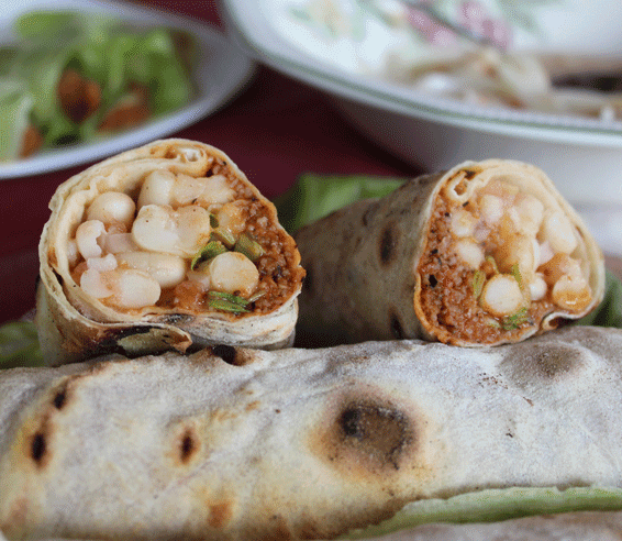 Durum kebab vegano cortado por la mitad, relleno de alubias blancas, salsa especiada y verduras frescas, envuelto en pan durum casero.