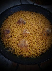 Vista cenital de una paellera individual con arroz, carne de conejo y el fumet a punto de evaporarse para formar el socarrat.