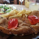 Cachopo asturiano crujiente relleno de queso, servido con patatas fritas y ensalada fresca.