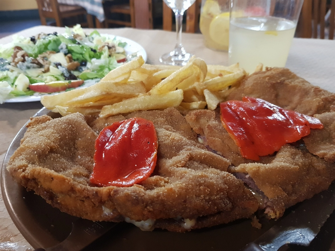 Cachopo asturiano crujiente relleno de queso, servido con patatas fritas y ensalada fresca.