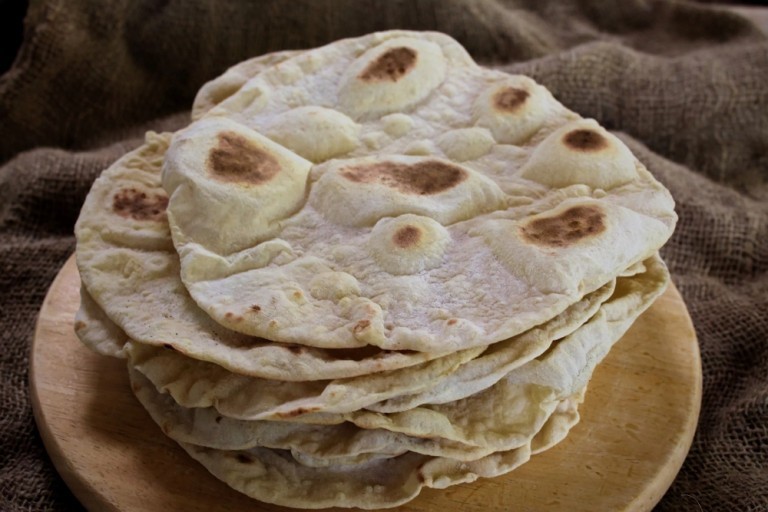 Pan durum casero apilado sobre madera, con textura dorada y cocido en sartén sin aceite.