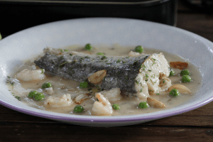 Merluza en salsa verde con gambas 3 Detalle de un lomo de merluza en salsa verde con gambas y guisantes en primer plano.