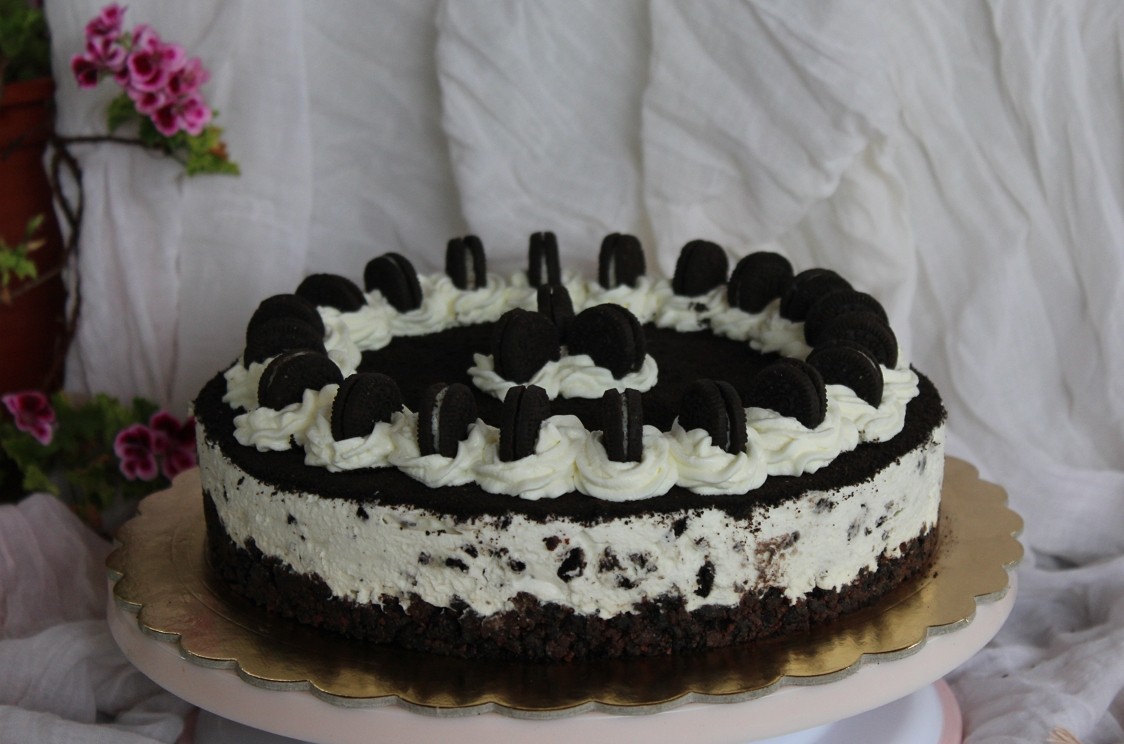 Tarta de queso Cheesecake de Oreo sin horno decorada con nata y galletas sobre un soporte blanco.
